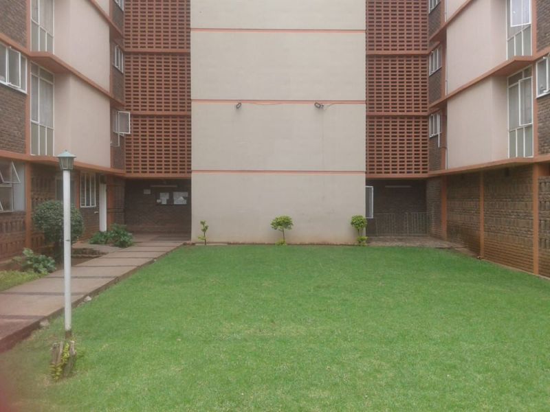 A view of the rear courtyard area featuring a central lawn, paved walkways, and brick apartment building facades with decorative breeze block ventilation screens.