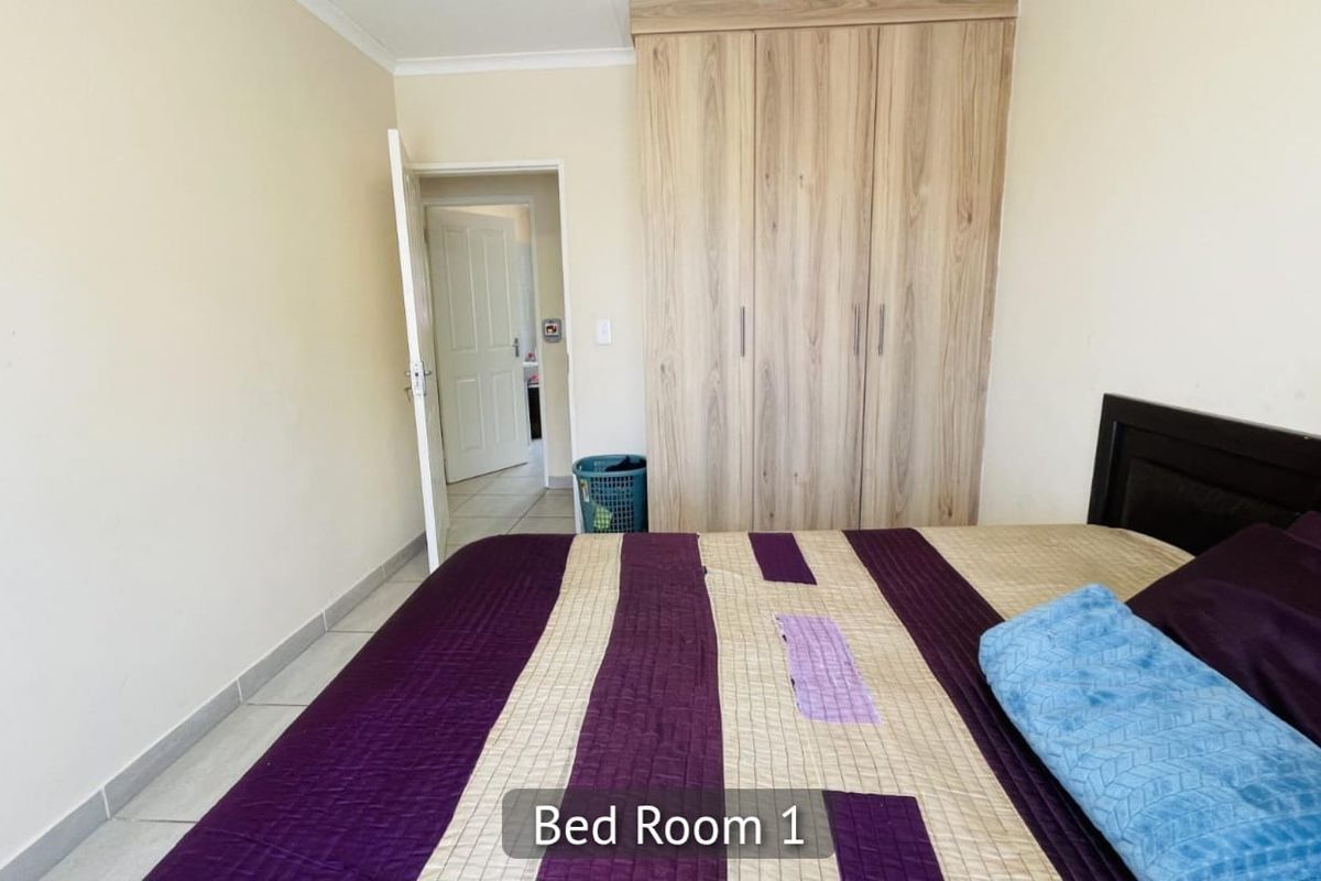 A bedroom featuring built-in wooden cupboards and tiled flooring, with an adjacent doorway leading to another area of the home.