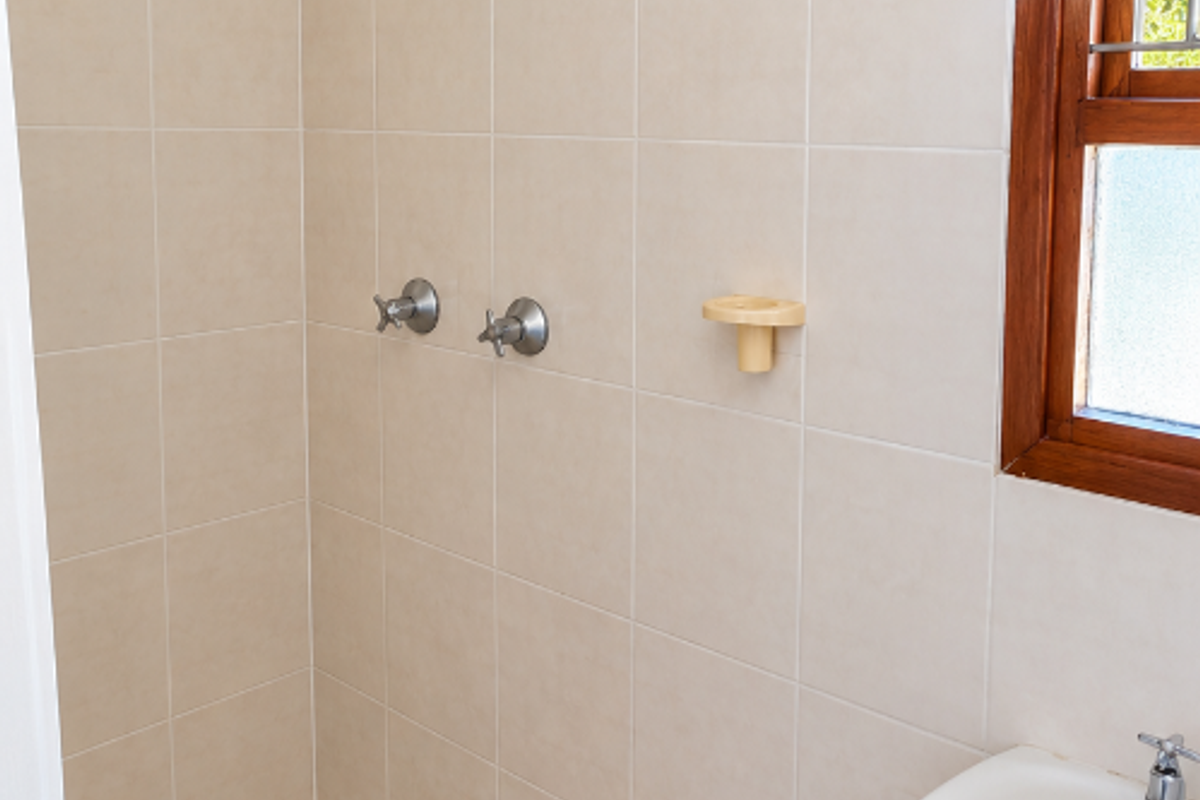 A functional bathroom featuring a tiled shower enclosure with a pedestal basin and natural light from a timber-framed window.