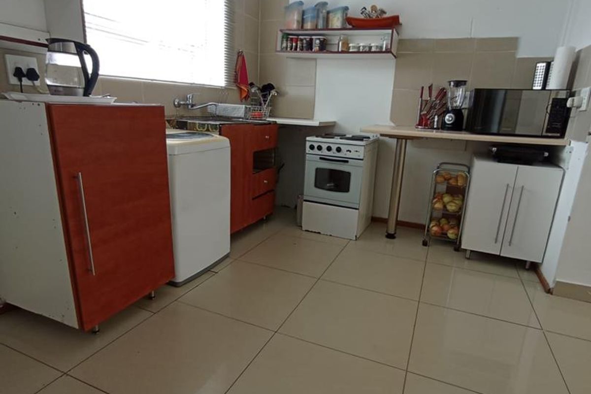 A functional kitchen featuring tiled flooring, built-in cabinetry, a freestanding stove, and a tiled backsplash with a large window for natural light.