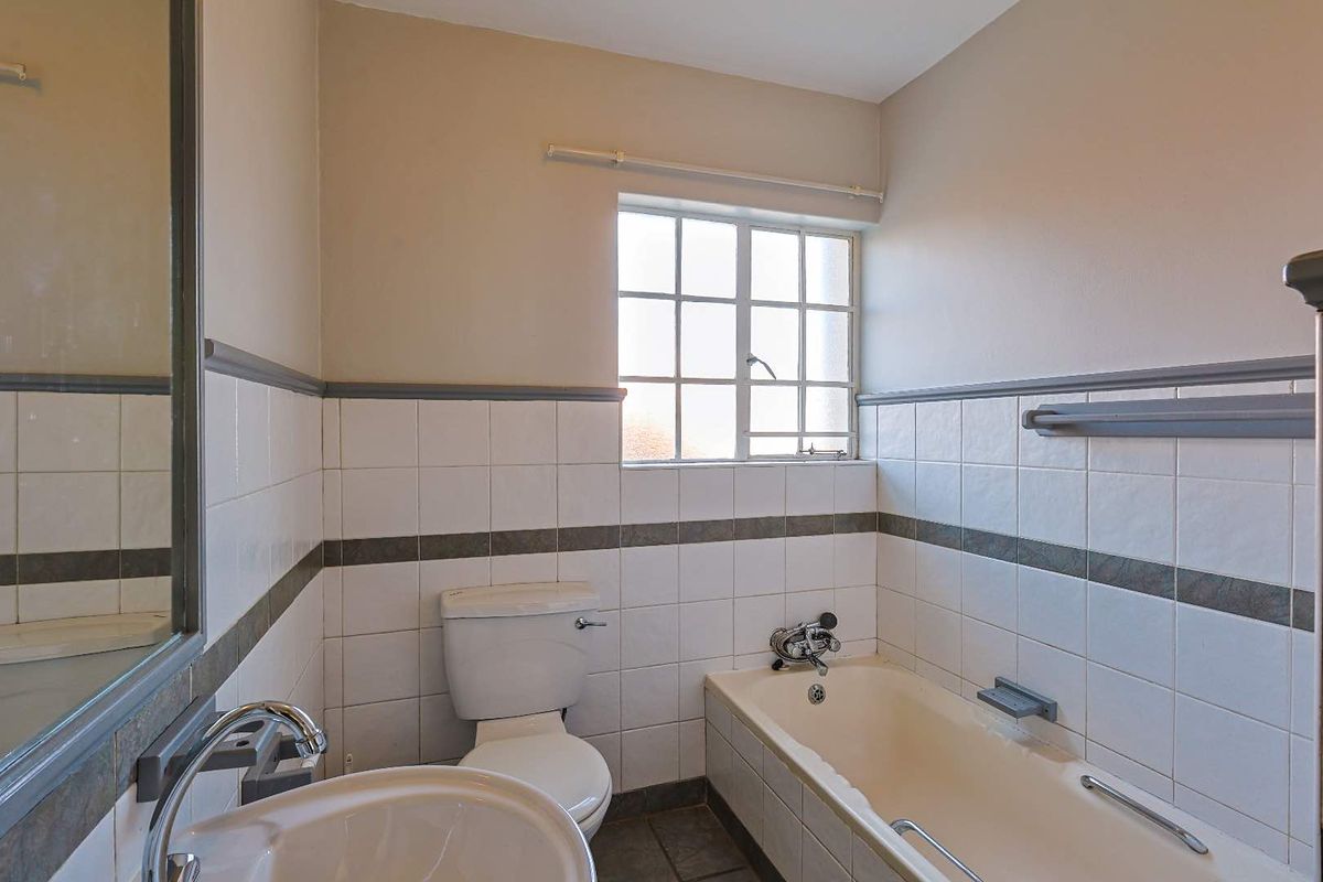 A functional bathroom featuring a bathtub, toilet, and pedestal sink with tiled walls and a window for natural light.