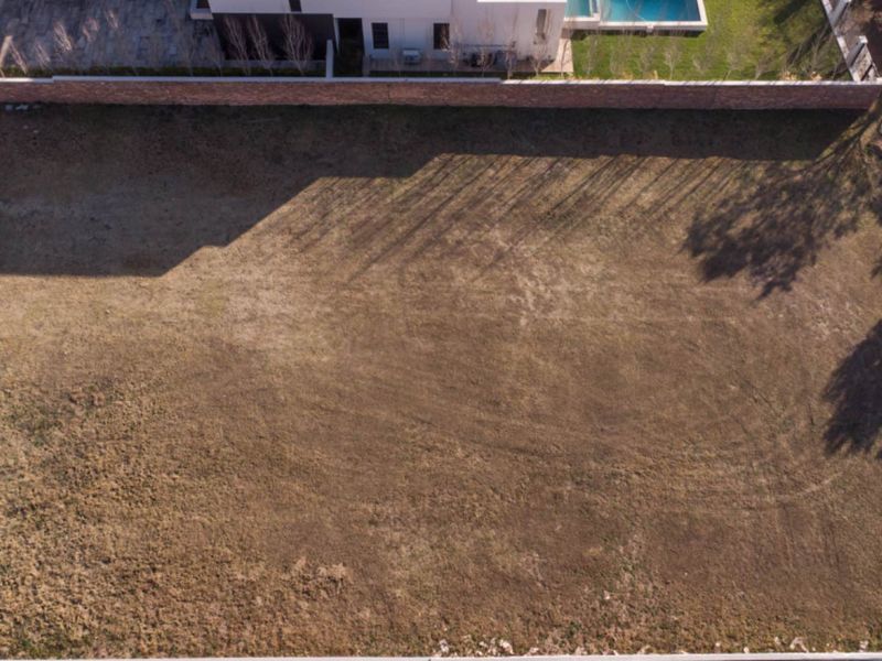 Aerial view of a vacant residential plot featuring a boundary wall and adjacent developed property.