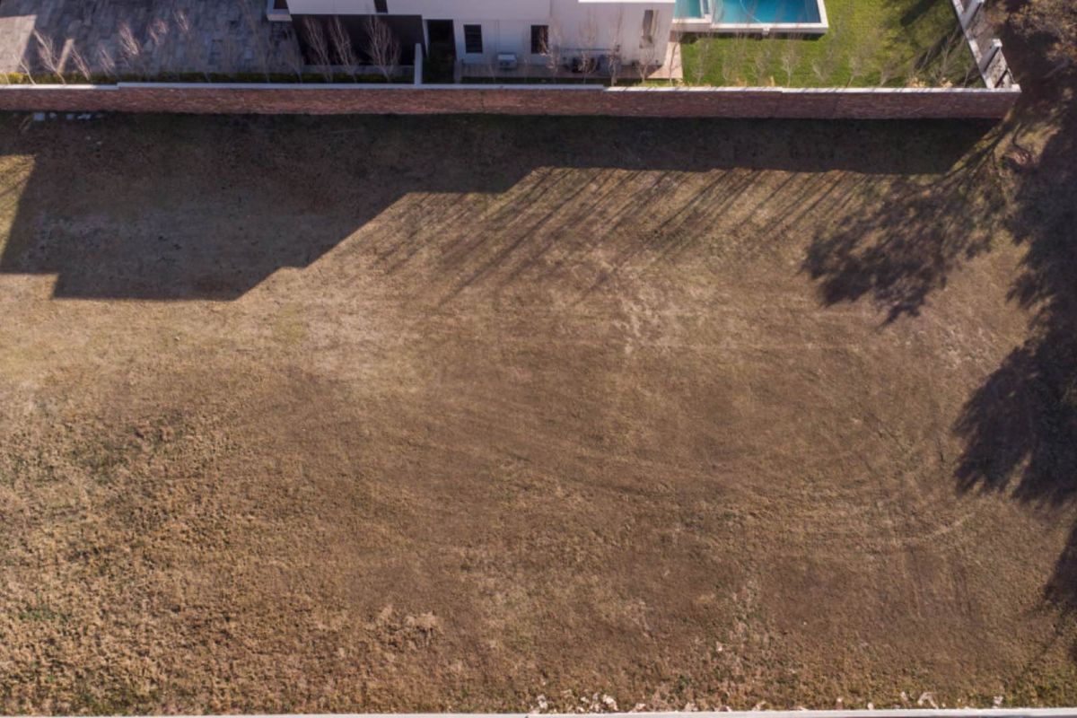 Aerial view of a vacant residential plot featuring a boundary wall and adjacent developed property.