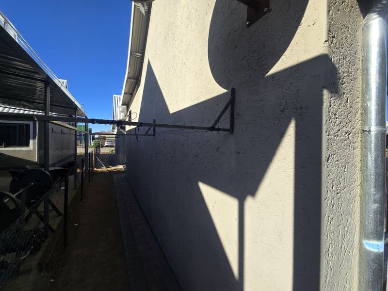 A side exterior view of the property featuring a paved walkway, wall-mounted clothesline, and metal downpipe along the building facade.