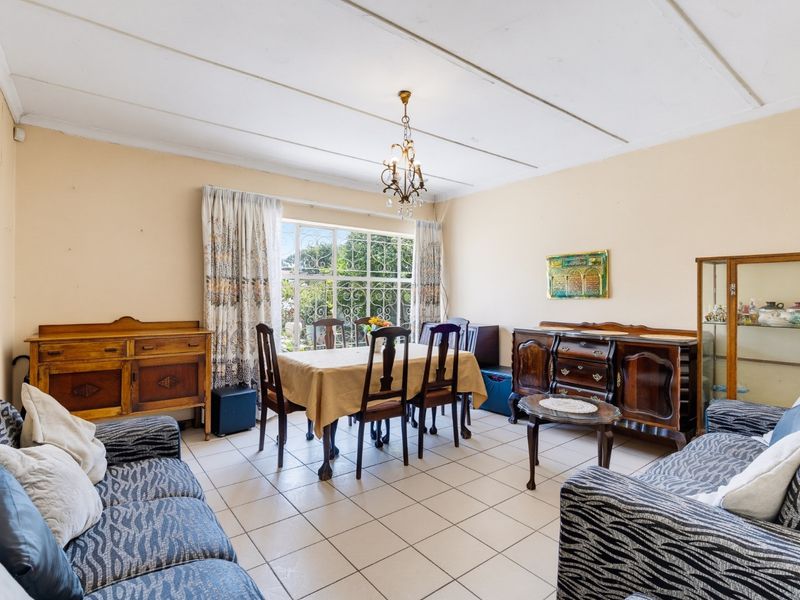 Open plan living and dining area featuring tiled flooring, large window with security bars, and a central chandelier.