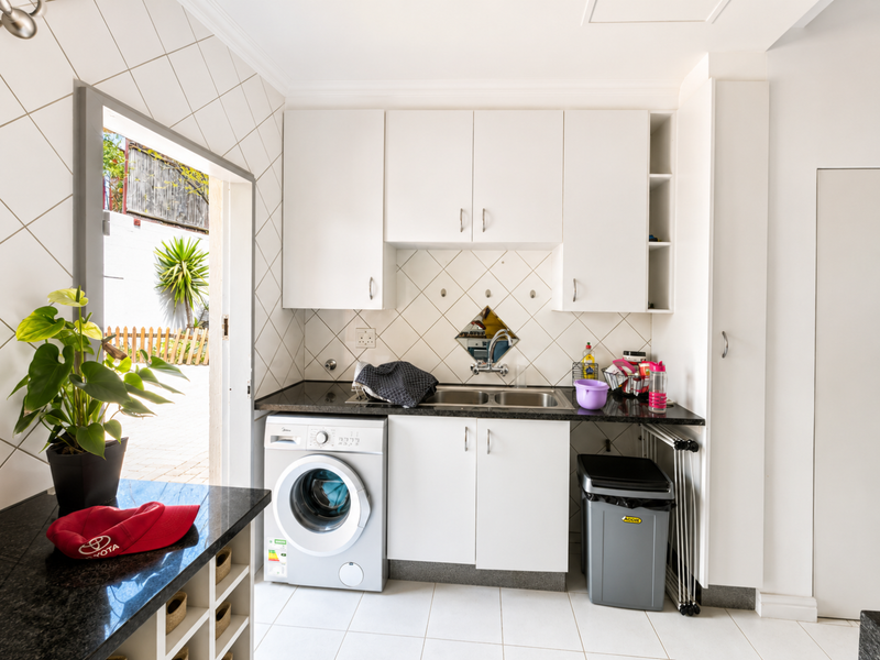 A functional laundry area featuring white built-in cabinetry, a double sink with granite countertops, tiled backsplash, and dedicated space for a washing machine.