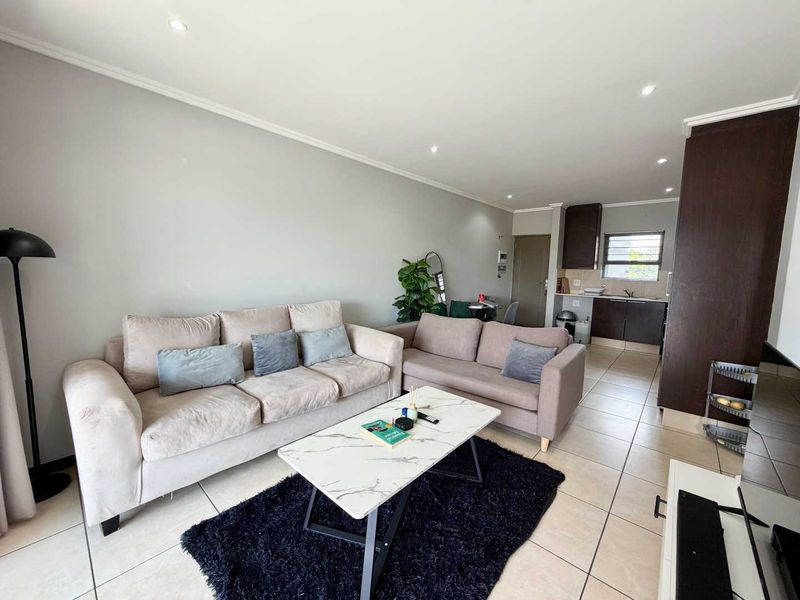 An open-plan living area featuring tiled flooring, recessed lighting, and a compact kitchen with built-in cabinetry and a sink.