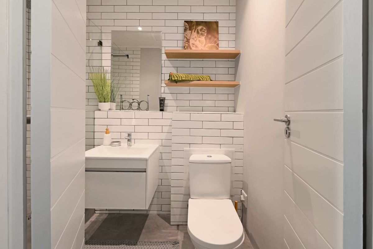 Modern bathroom featuring white subway tile walls, a wall-mounted vanity with a ceramic basin, and a sleek back-to-wall toilet.