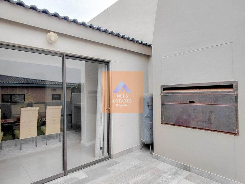 Covered patio area featuring a built-in braai, tiled flooring, and large sliding glass doors providing access to the interior living space.