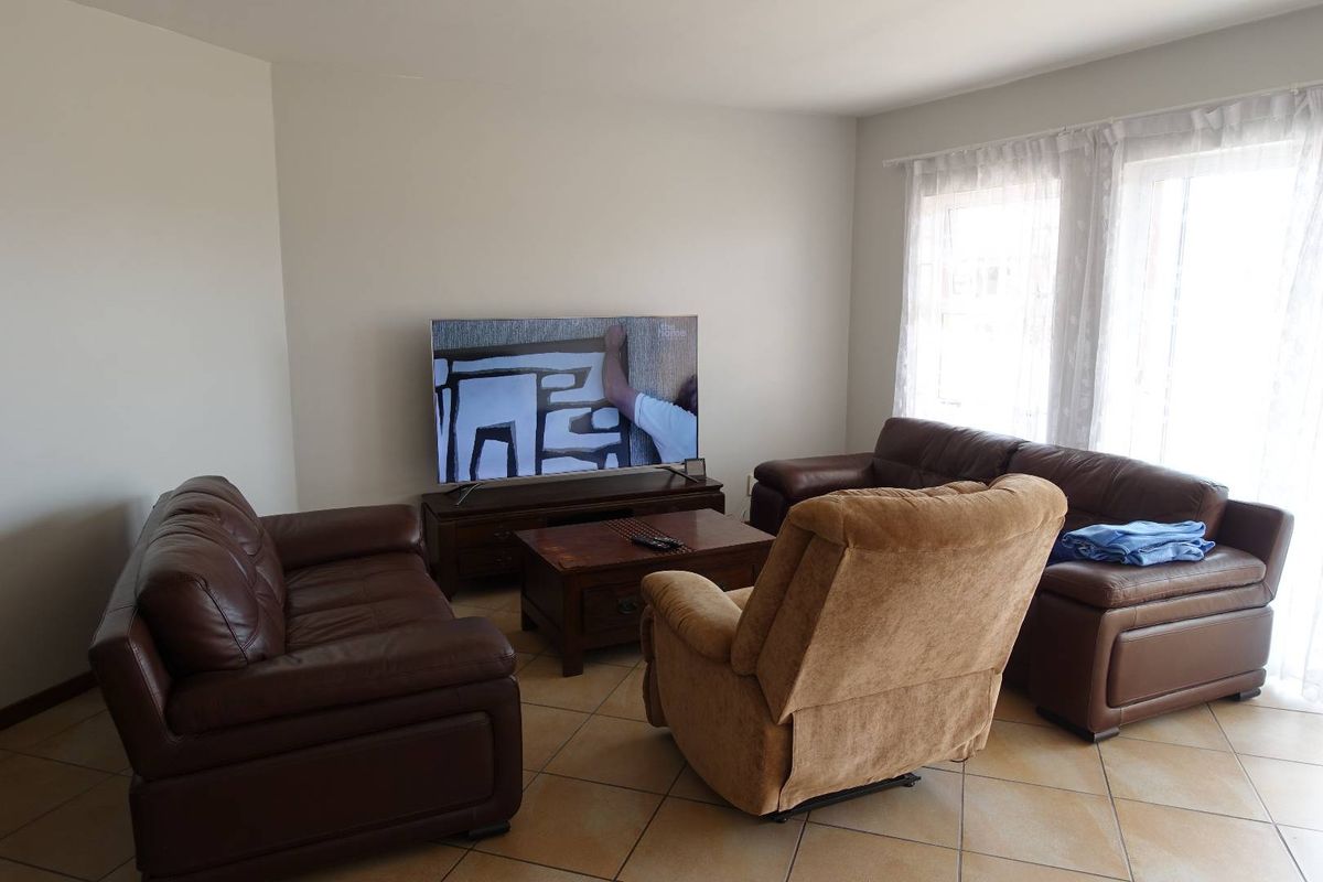 A comfortable living room featuring neutral wall tones, tiled flooring, and a large sliding glass door that provides natural light.