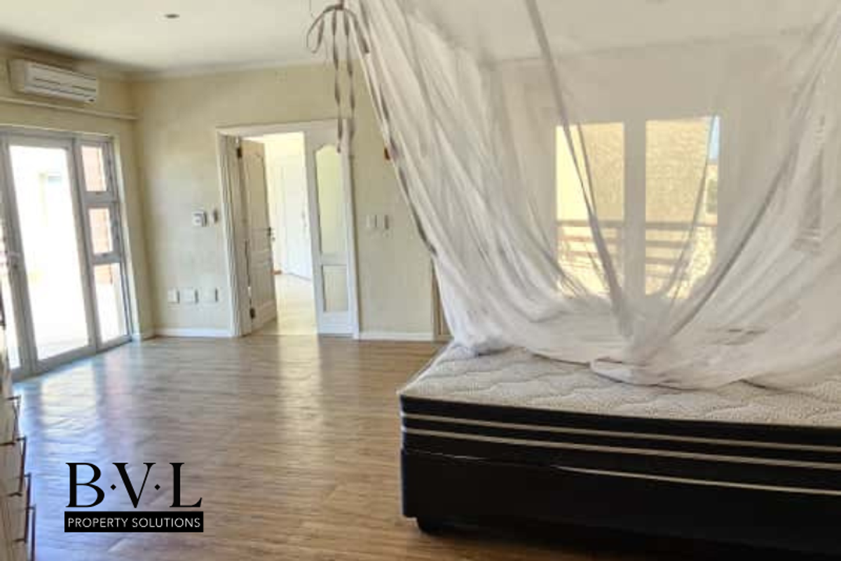 Spacious bedroom featuring wood-look flooring, wall-mounted air conditioning unit, and direct access to an outdoor area through glass sliding doors.