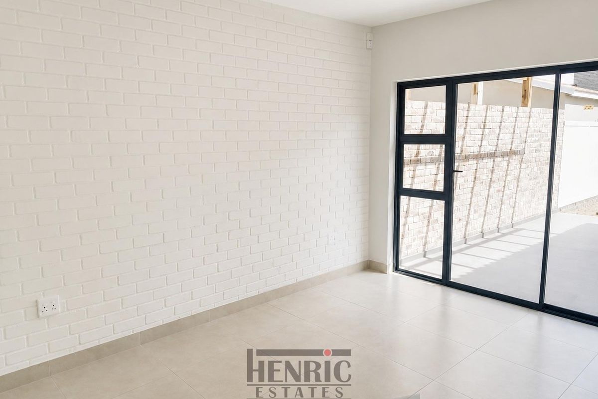 A bright, empty living area featuring a white painted brick feature wall, modern tiled flooring, and large sliding doors leading to an outdoor space.
