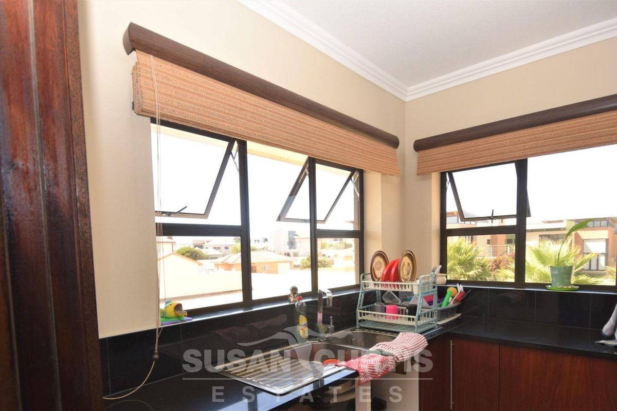 A functional kitchen area featuring dark cabinetry, black granite countertops, a stainless steel sink, and large windows providing natural light.