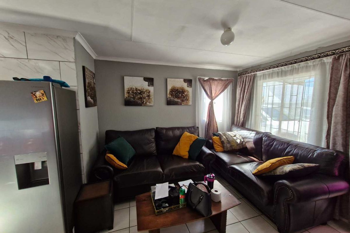 A cozy living room featuring tiled flooring, large windows with curtains, and neutral wall finishes, providing a comfortable and functional living space.