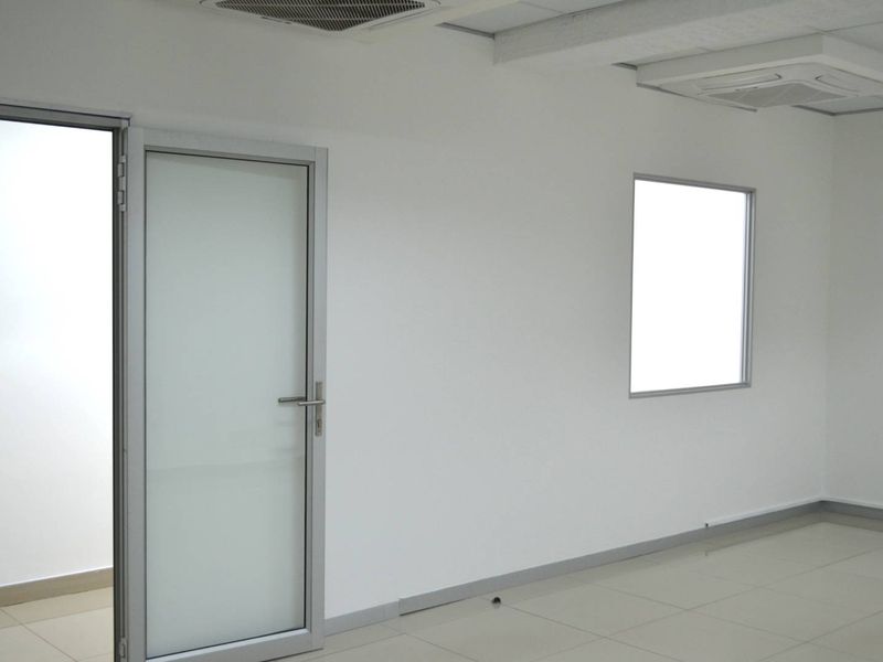 A clean, empty office space featuring tiled flooring, an aluminium framed glass door, and a built-in ceiling air conditioning unit.