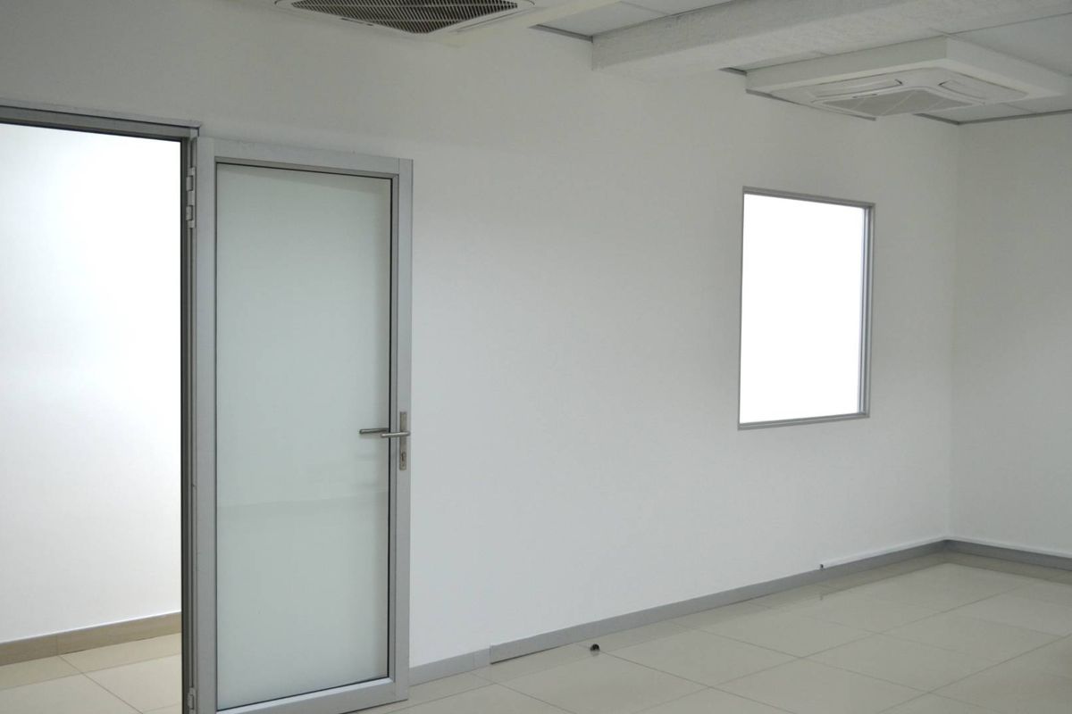 A clean, empty office space featuring tiled flooring, an aluminium framed glass door, and a built-in ceiling air conditioning unit.