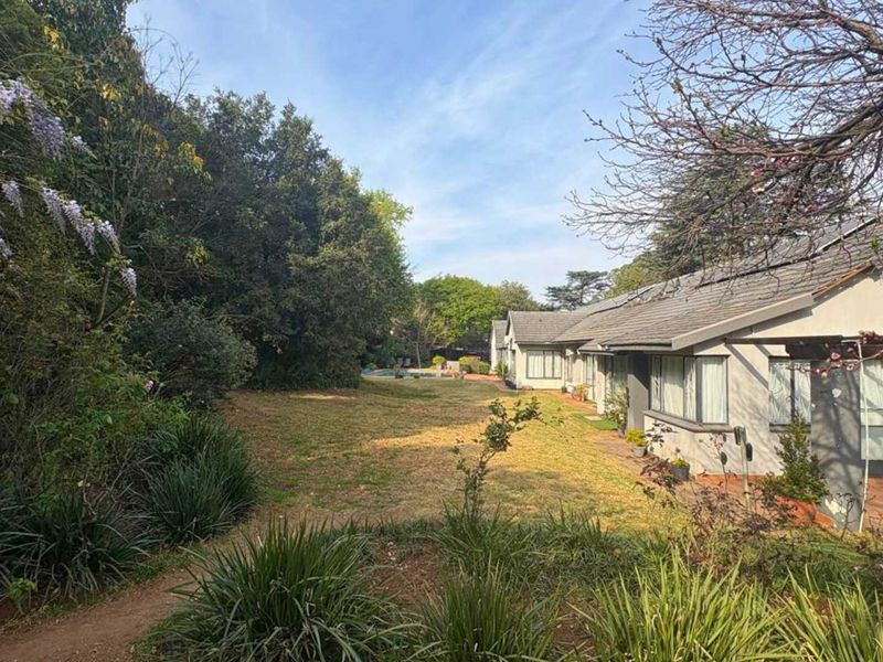 A view of the rear elevation featuring a tiled roof with solar panels, a covered patio area, and a spacious landscaped garden.
