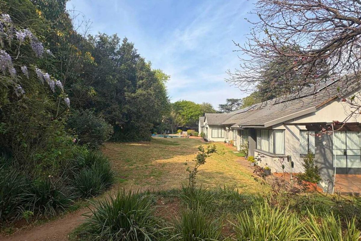 A view of the rear elevation featuring a tiled roof with solar panels, a covered patio area, and a spacious landscaped garden.