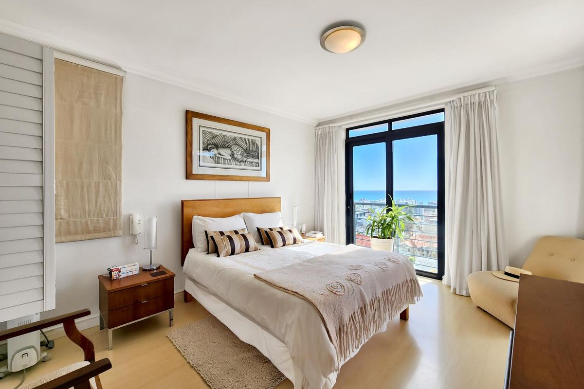 A bright and well-maintained bedroom featuring laminate flooring, a ceiling light fixture, and a sliding glass door leading to a balcony with ocean views.