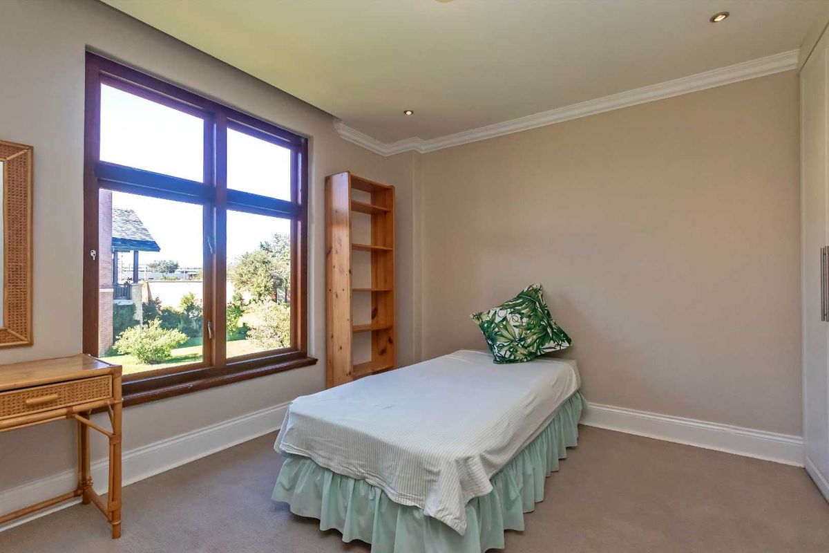 A bright bedroom featuring neutral carpeting, crown molding, recessed lighting, and large wooden-framed windows overlooking the garden.