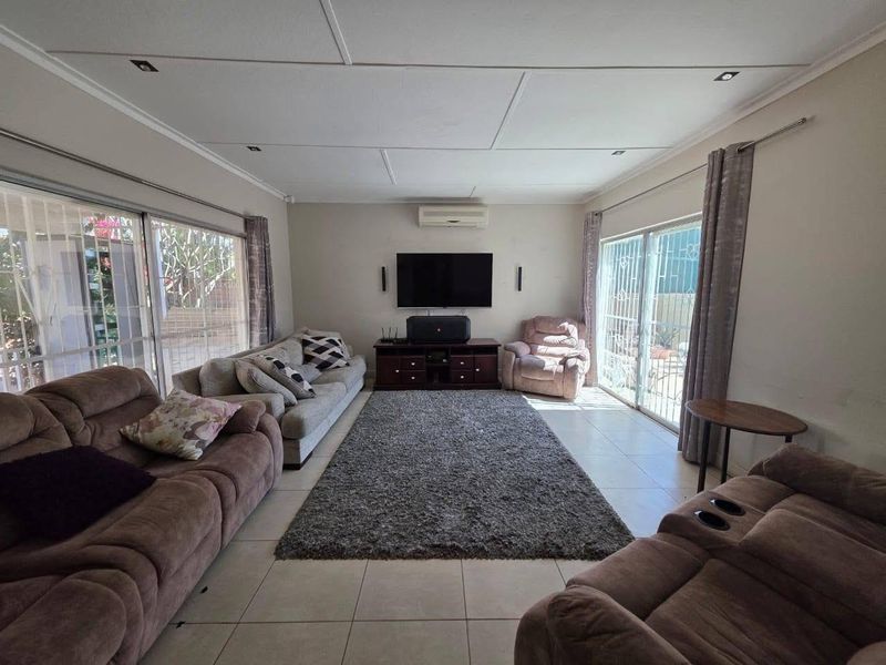 Spacious living room featuring tiled flooring, recessed ceiling lighting, a wall-mounted air conditioning unit, and large sliding glass doors with security gates.