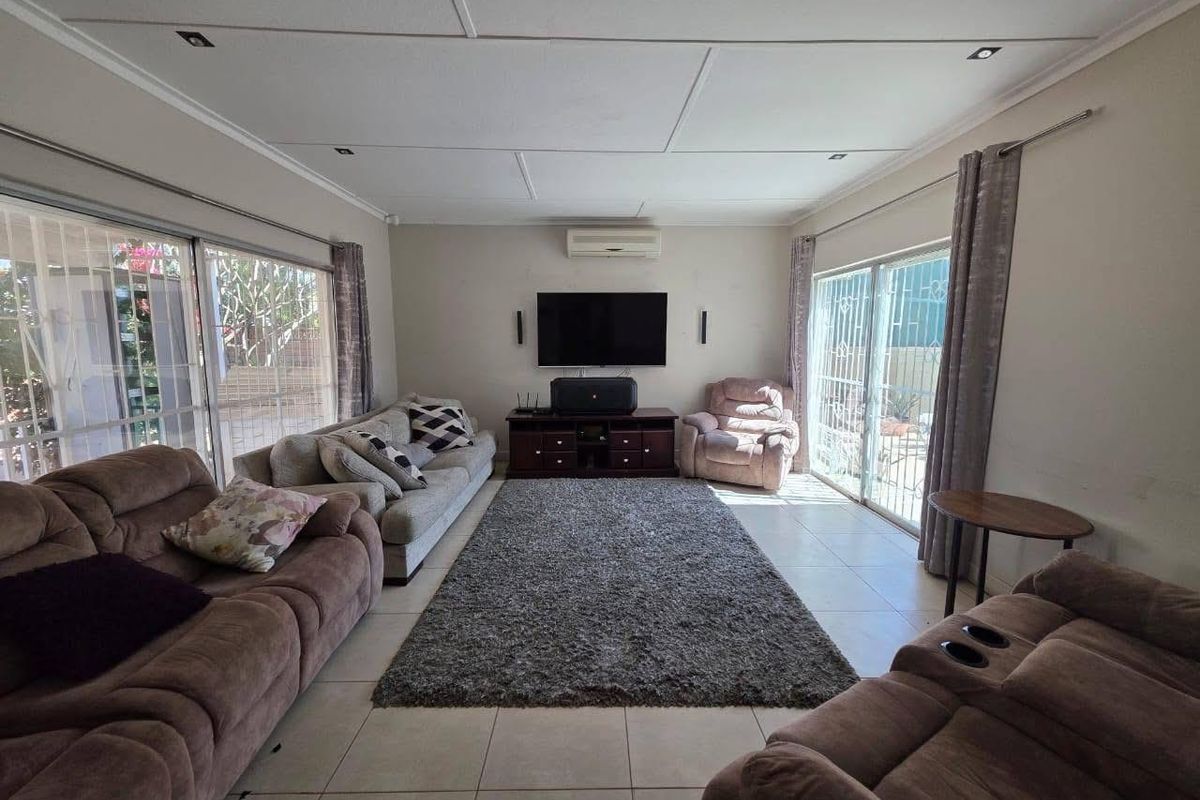 Spacious living room featuring tiled flooring, recessed ceiling lighting, a wall-mounted air conditioning unit, and large sliding glass doors with security gates.