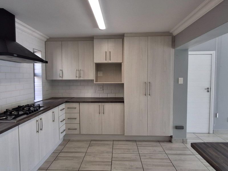 Modern kitchen featuring light wood-finish cabinetry, dark laminate countertops, a gas hob with extractor fan, and neutral tiled flooring.