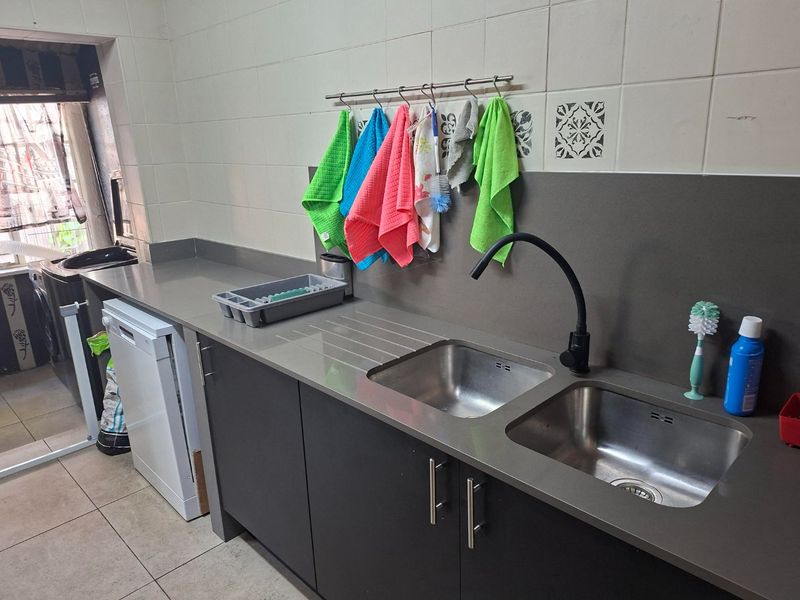 A functional laundry area featuring dark grey cabinetry, a double stainless steel sink with a modern black mixer tap, and tiled splashback.