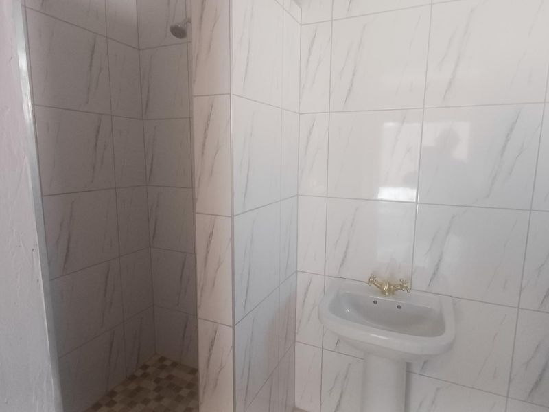 A functional bathroom featuring a pedestal basin and a tiled shower enclosure with marble-effect wall tiles.