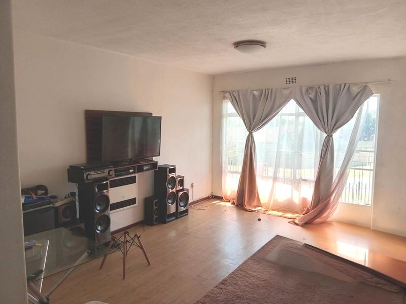 A living room featuring laminate flooring, a wall-mounted heater, and a large sliding glass door providing natural light.