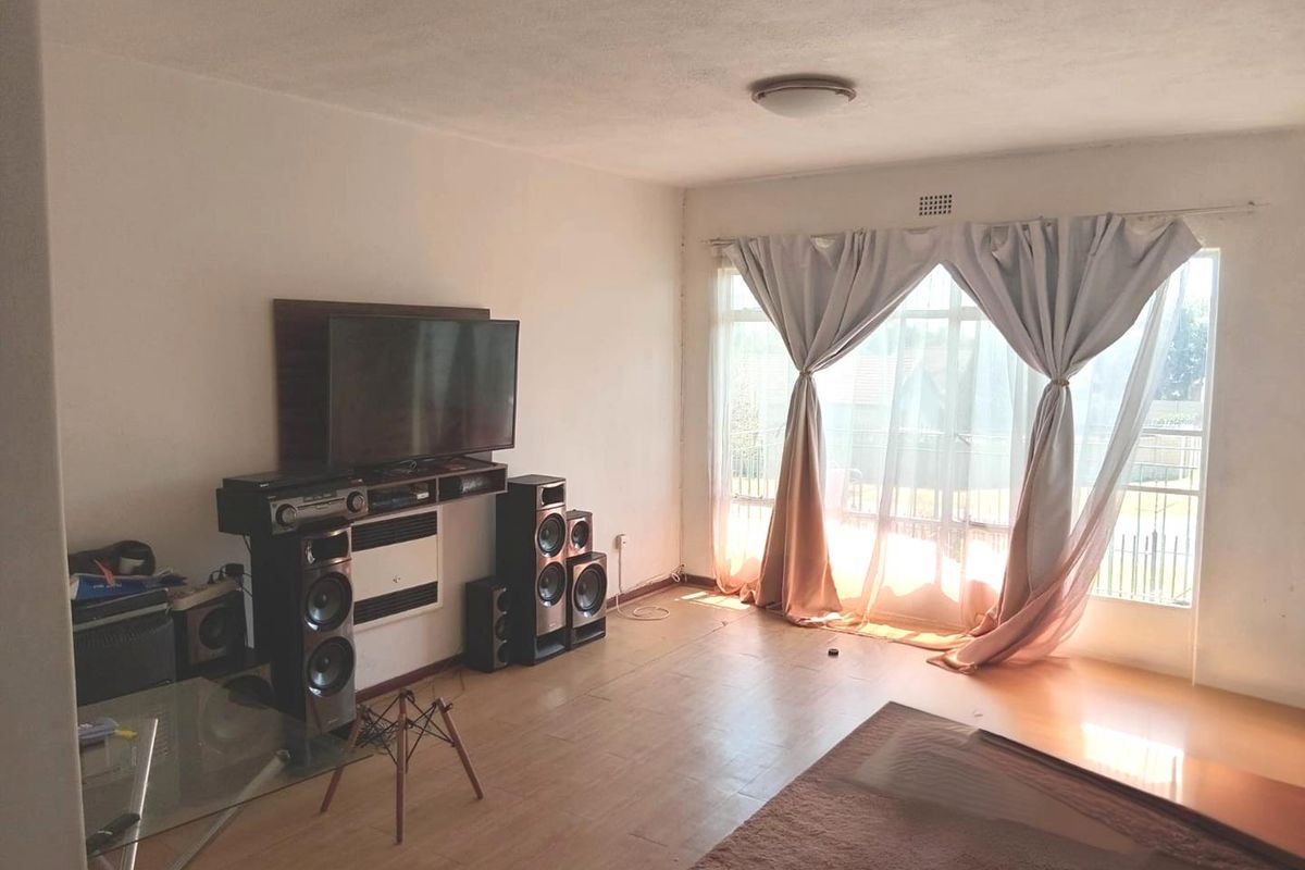 A living room featuring laminate flooring, a wall-mounted heater, and a large sliding glass door providing natural light.