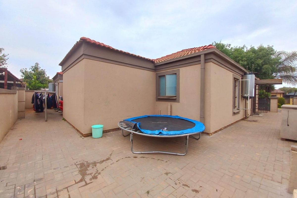 Rear exterior view of the property featuring paved courtyard area, perimeter wall, and external geyser unit.