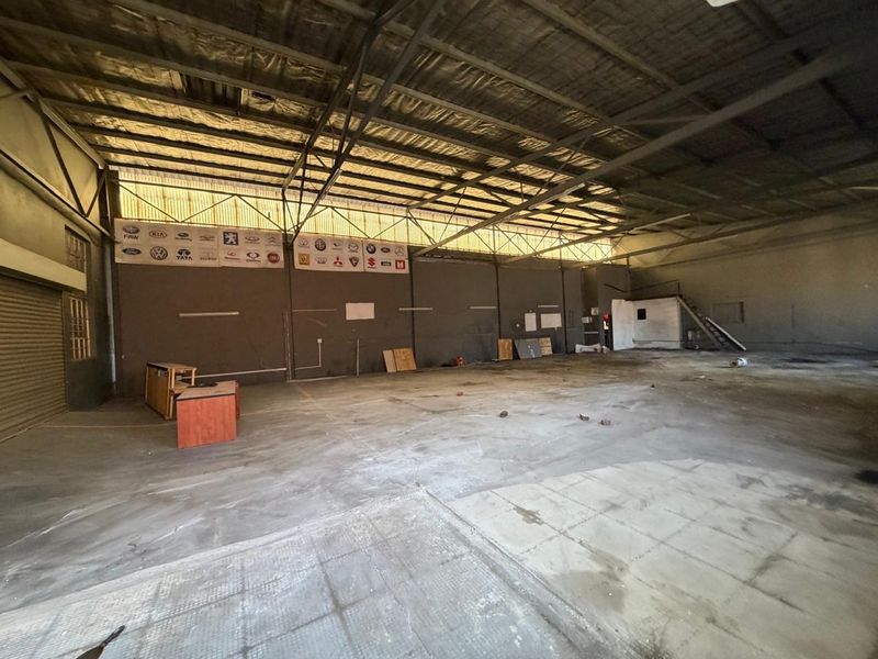 Spacious industrial utility area featuring high exposed steel ceilings, concrete flooring, and a roller shutter door, suitable for workshop or storage use.