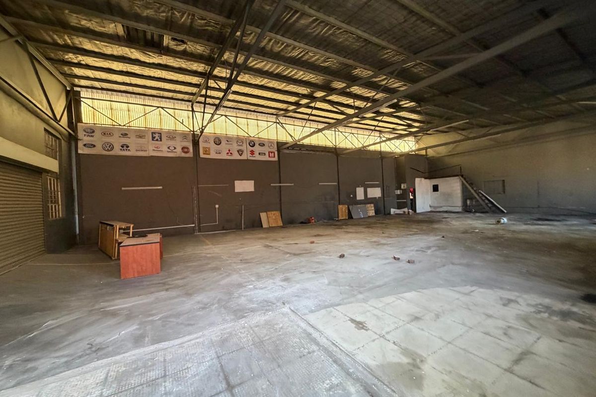 Spacious industrial utility area featuring high exposed steel ceilings, concrete flooring, and a roller shutter door, suitable for workshop or storage use.