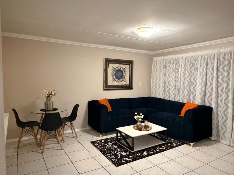 A well-maintained living room featuring neutral wall tones, tiled flooring, and classic ceiling cornice detailing, providing a comfortable and functional living space.