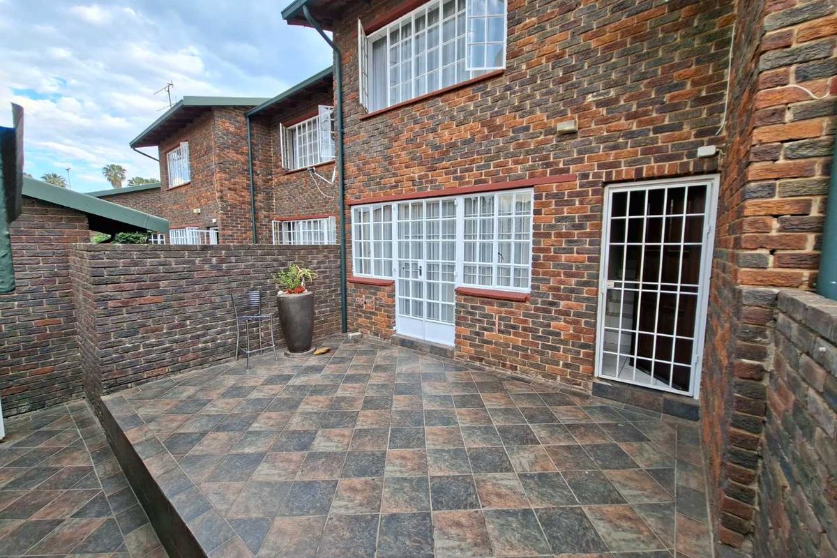 A private rear patio area featuring durable tiled flooring, face brick exterior walls, and secure access points with fitted security gates.