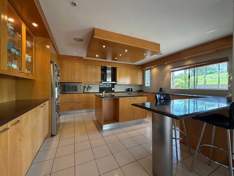 Spacious kitchen featuring extensive wooden cabinetry, granite countertops, a central island, breakfast bar, and integrated appliances with recessed lighting.