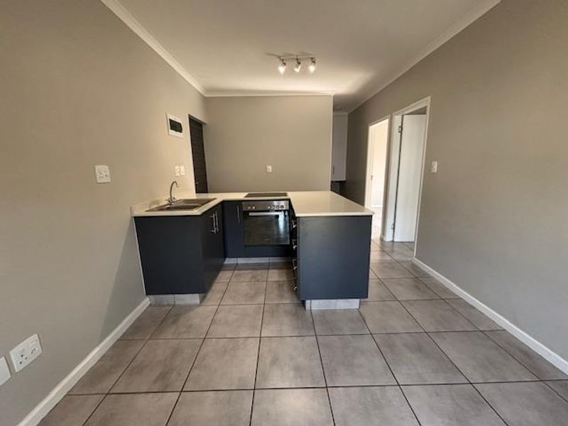 A modern, clean kitchen featuring dark cabinetry, stone countertops, a built-in oven, and an electric hob, set against neutral grey walls and tiled flooring.