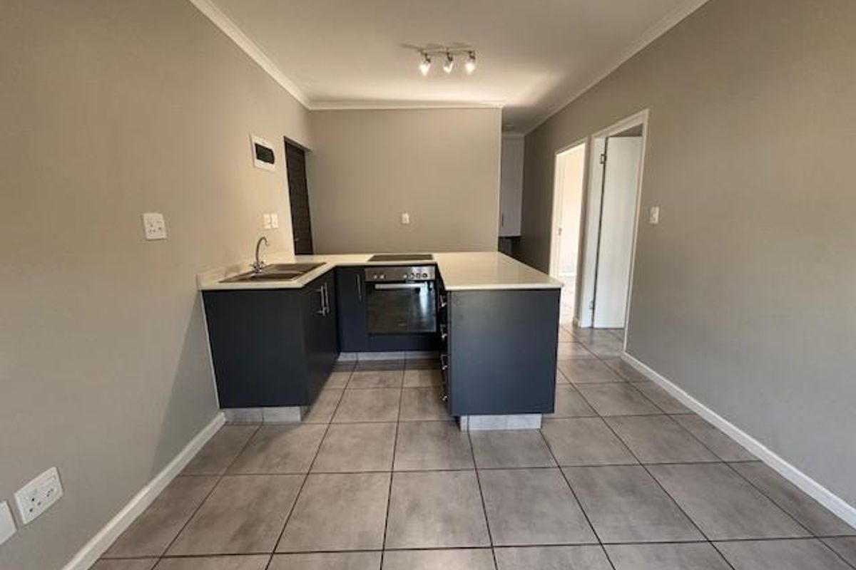 A modern, clean kitchen featuring dark cabinetry, stone countertops, a built-in oven, and an electric hob, set against neutral grey walls and tiled flooring.