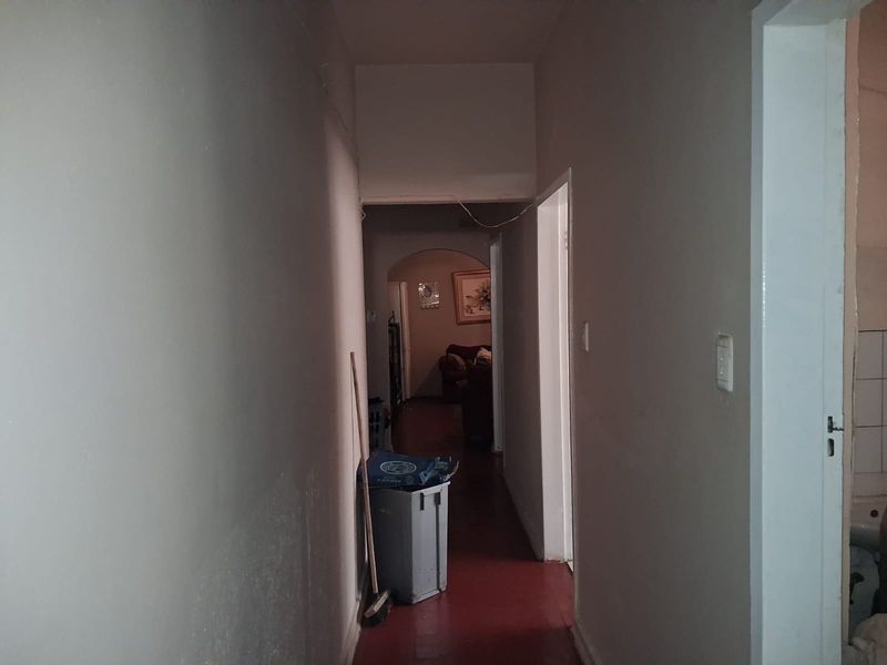 A narrow interior hallway featuring an arched transition and painted flooring, requiring cosmetic updates to the wall finishes.