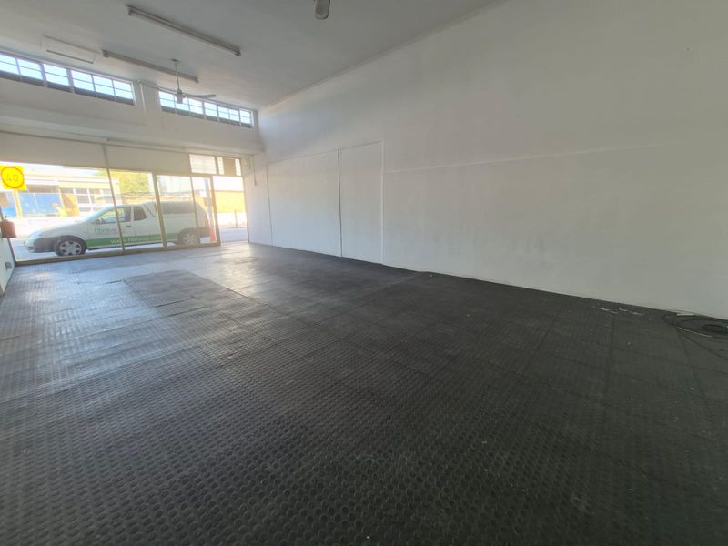 A spacious, empty open-plan commercial unit featuring durable rubber flooring, large glass storefront windows, and functional overhead lighting.