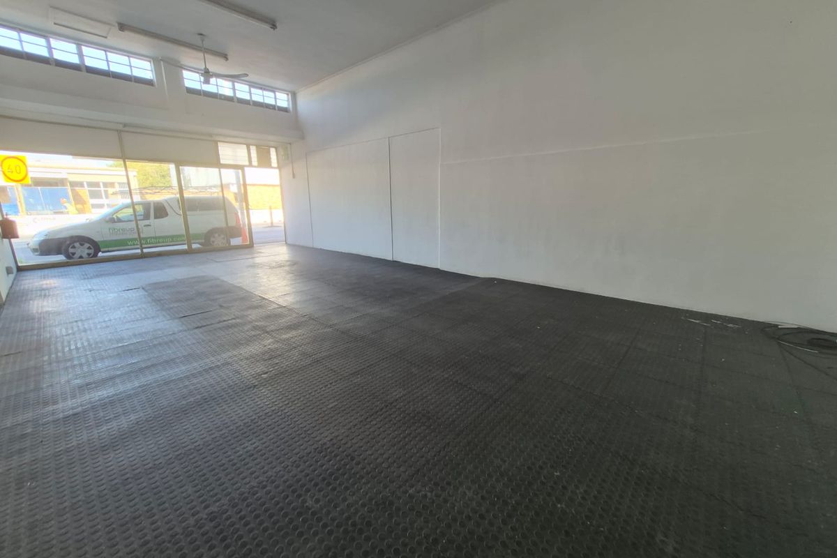 A spacious, empty open-plan commercial unit featuring durable rubber flooring, large glass storefront windows, and functional overhead lighting.