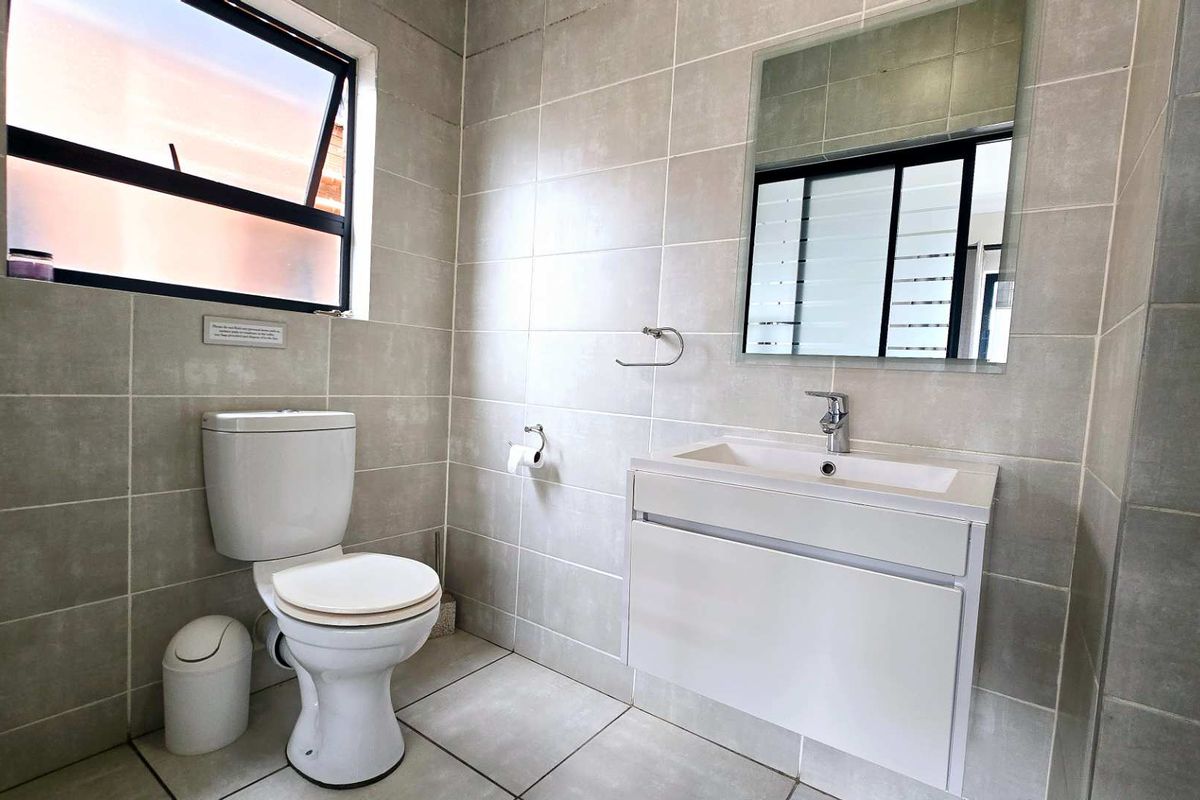 Modern bathroom featuring neutral wall and floor tiles, a wall-mounted vanity with basin, and a functional top-hung window for natural ventilation.