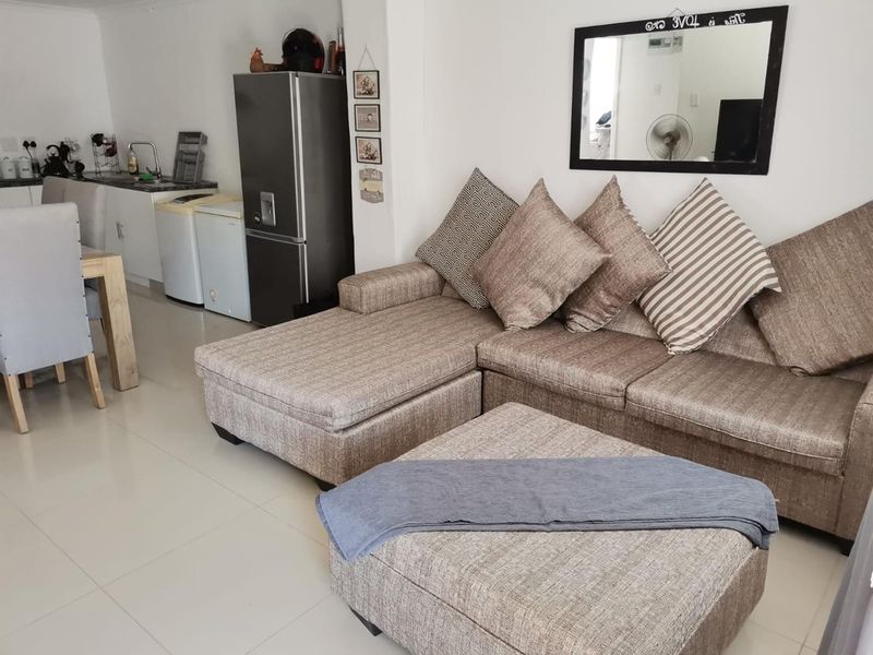 Open-plan living and dining area featuring tiled flooring and a compact kitchen corner with built-in cabinetry and sink.