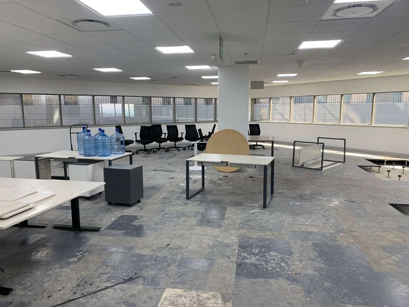 Open-plan office space featuring a suspended ceiling, recessed lighting, and large windows, currently requiring flooring repairs and general refurbishment.