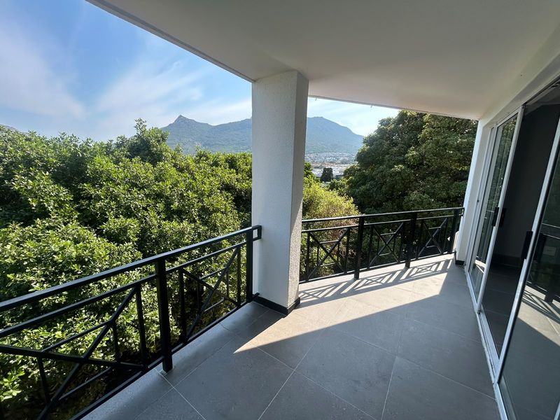 A spacious covered balcony featuring modern tiled flooring, a secure metal balustrade, and sliding glass doors, offering scenic mountain and treetop views.