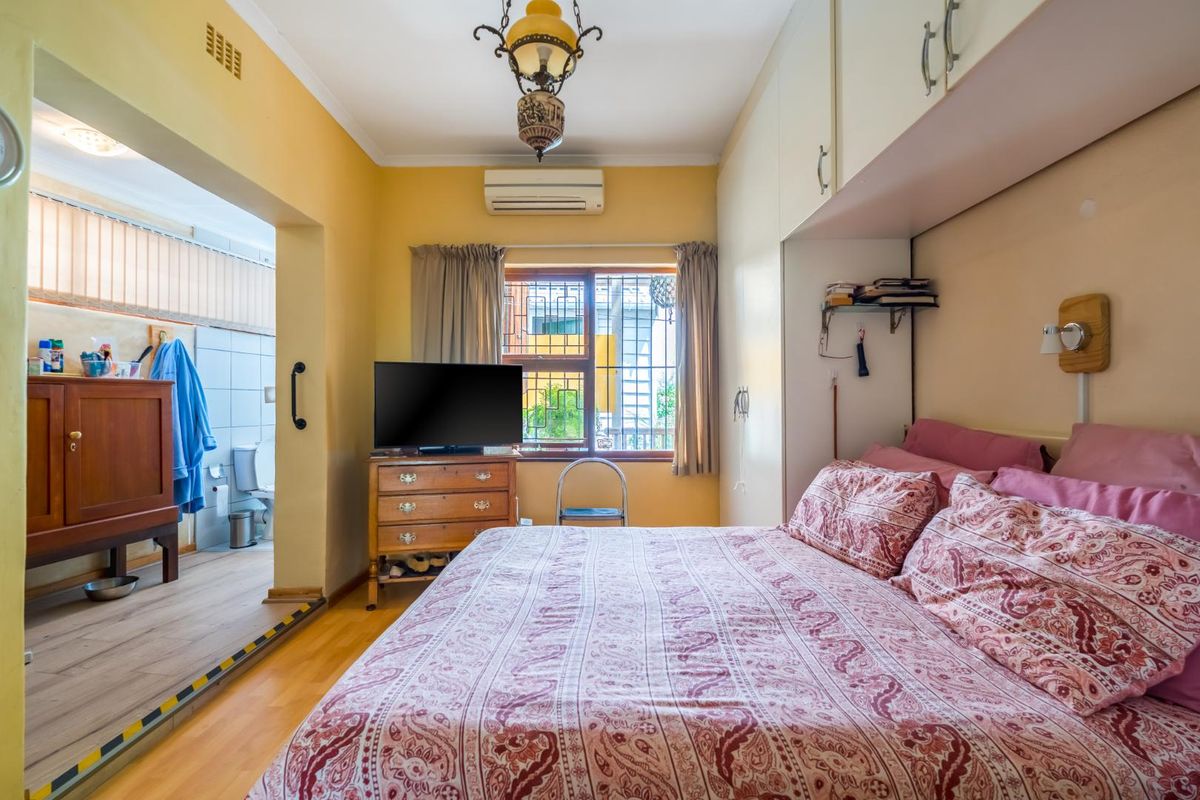 A bedroom featuring built-in cabinetry, a wall-mounted air conditioning unit, and an adjoining en-suite bathroom with tiled finishes.
