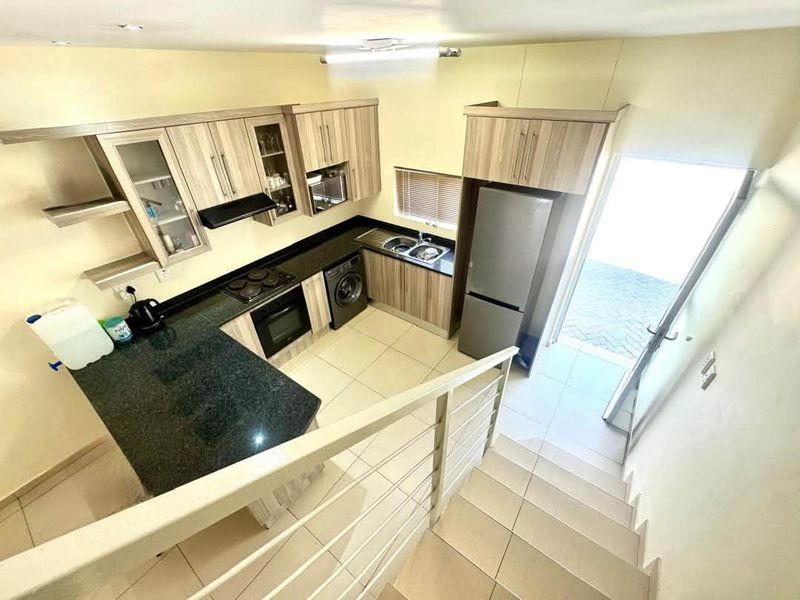 Modern kitchen featuring granite countertops, built-in cabinetry, integrated appliances, and tiled flooring, with direct access to an outdoor area via a staircase.