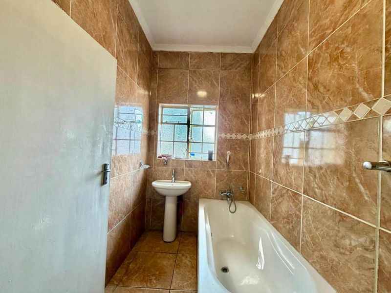 A functional bathroom featuring full-height wall tiling, a pedestal basin, and a standard bathtub with a window for natural light.