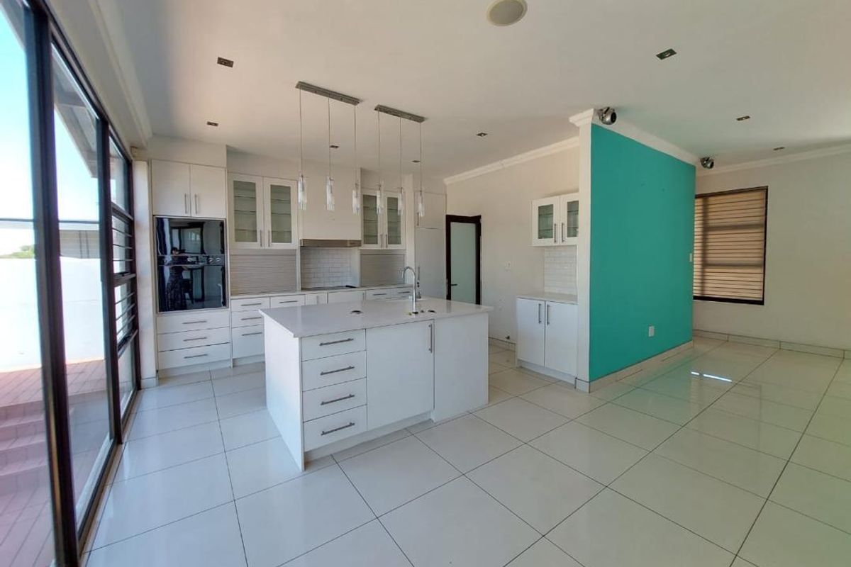 Modern kitchen featuring a central island, built-in oven, sleek white cabinetry, and large format floor tiles, offering a bright and functional culinary space.